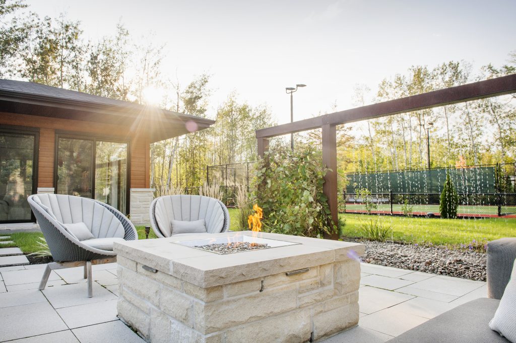 Cour arrière aménagée avec foyer extérieur, chaises et vue sur terrain de tennis à Boucherville